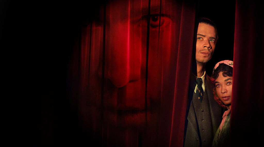 a man and a woman in between the dark curtains